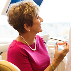 Senior woman in dental chair holding denture