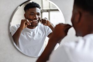 Young man flossing teeth while looking into mirror.